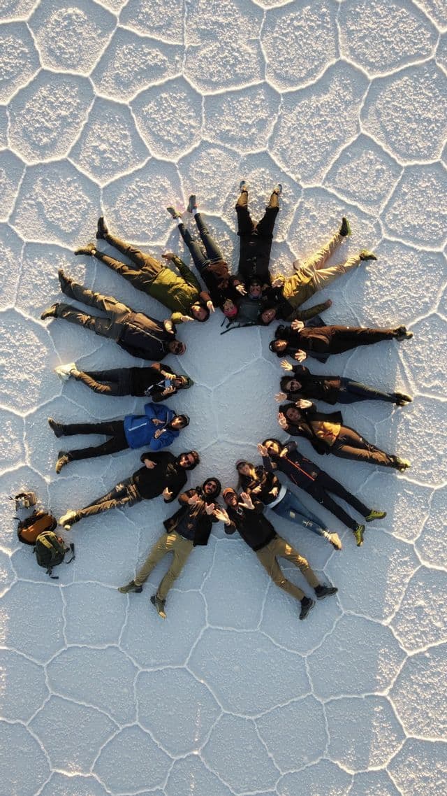 An aerial view of a WeRoad group trip lying in a circle on a vast salt flat with polygonal cracks.