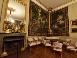 Corner of a room with tapestries on the walls and chairs around a circular table