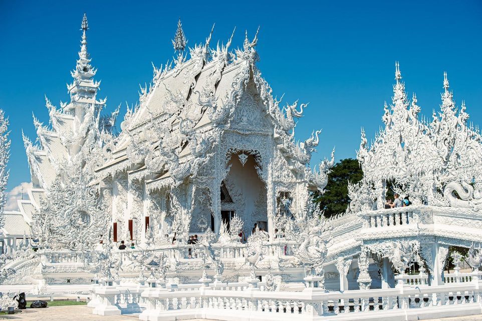 An ornate white temple with intricate carvings and spires stands under a clear blue sky.