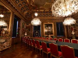 A long table with red chairs under various chandeliers in a gold room