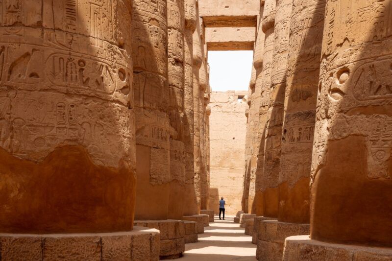 Sunlit corridor between rows of monumental, hieroglyph-covered columns in the Great Hypostyle Hall of the Temple of Karnak, Egypt.