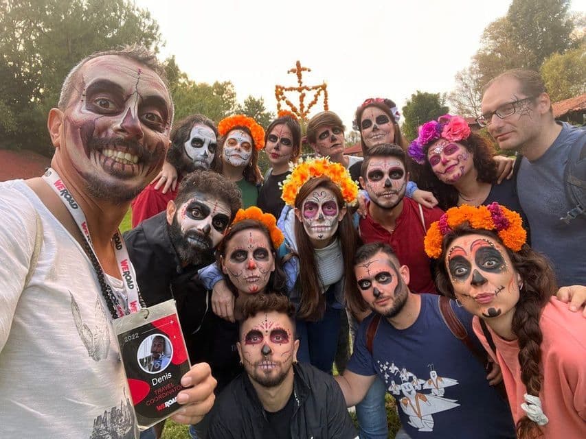 A WeRoad group trip poses for a selfie with their faces painted as Calavera skulls, some wearing flower crowns.
