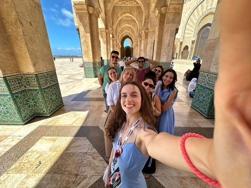 A WeRoad group trip smiles and poses for a selfie while standing in a line under an ornate arched colonnade.